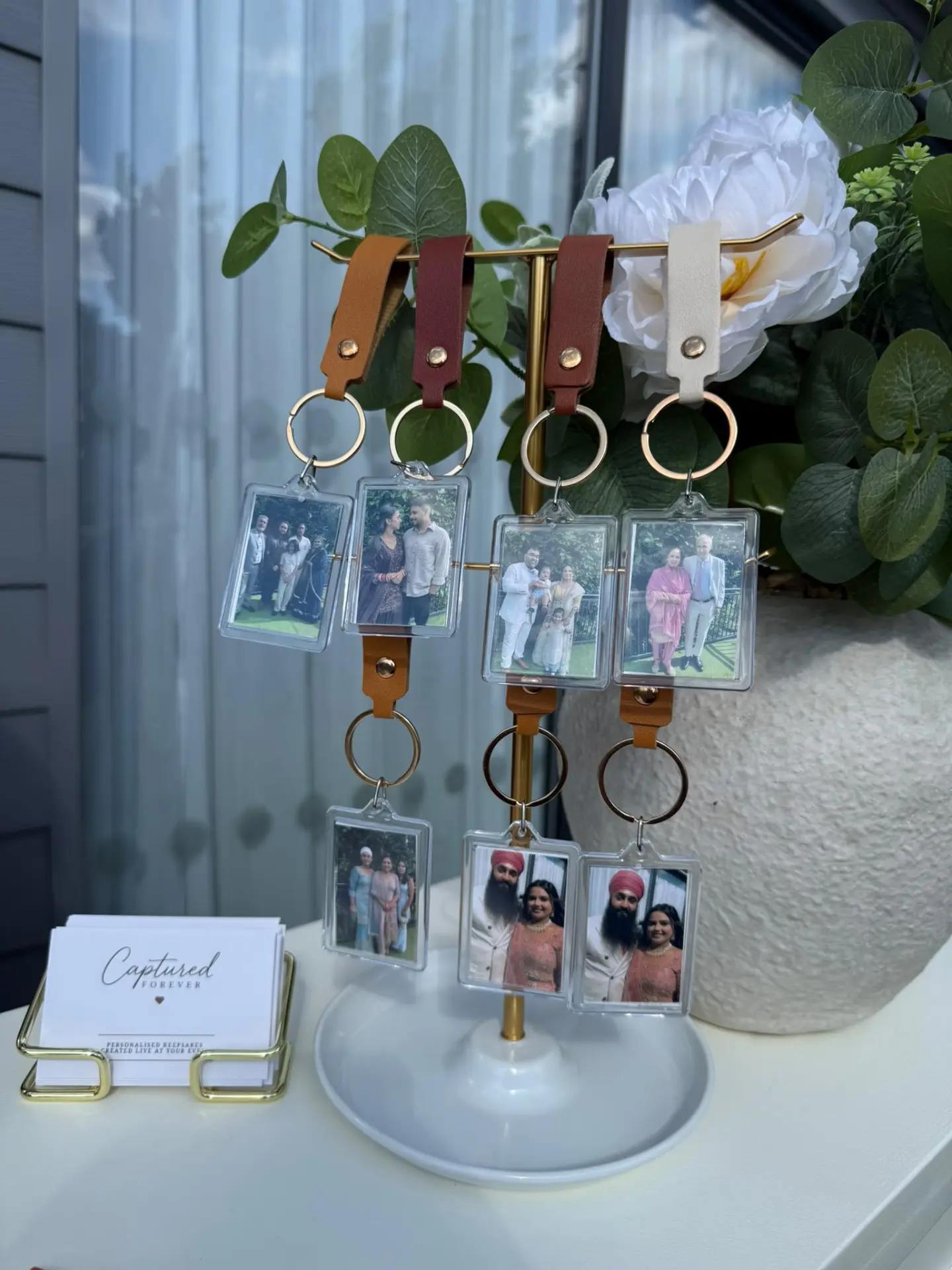Personalised photo keyrings hanging on a brass stand beside Captured Forever cards